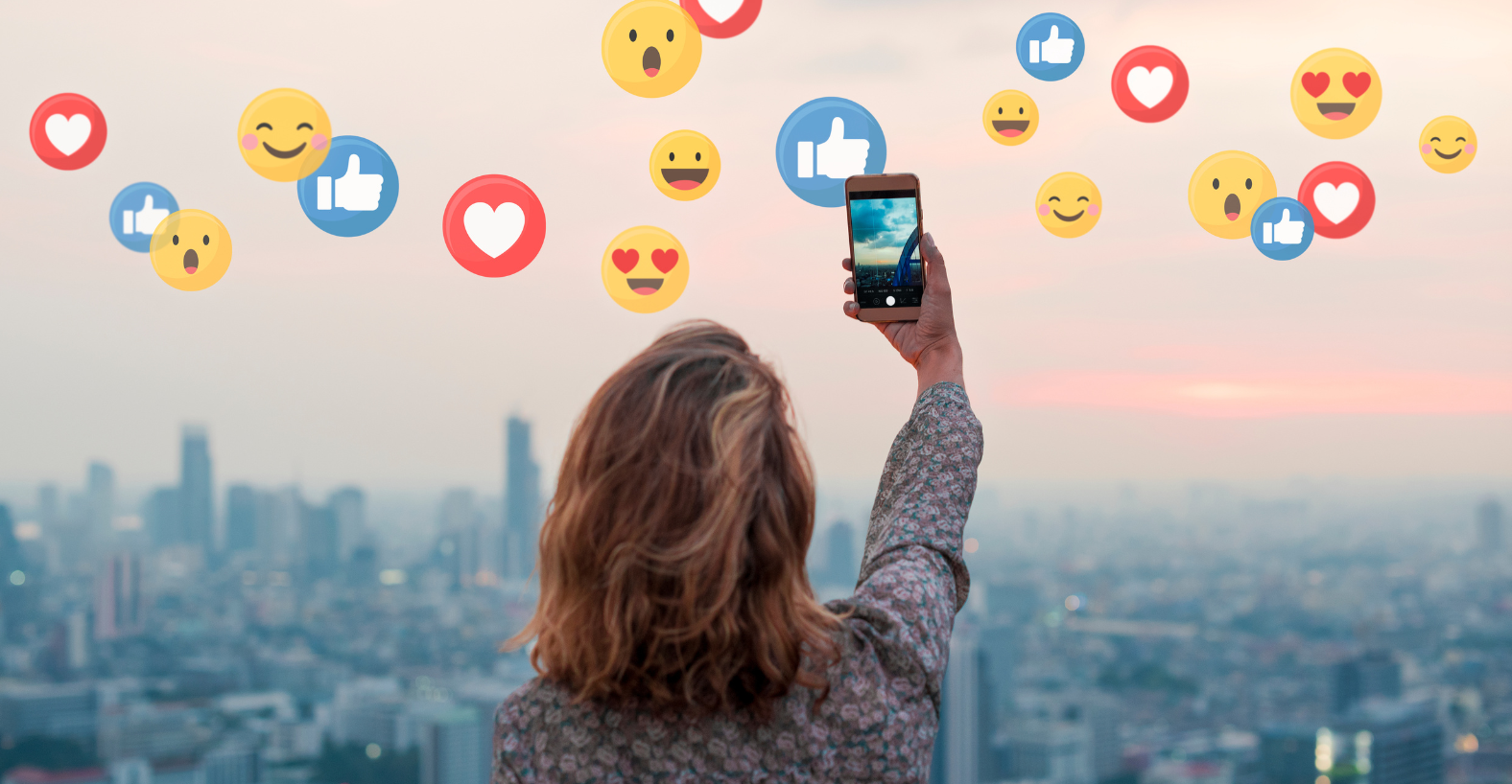 Person taking photo with smartphone, city skyline background, floating social media reaction emojis